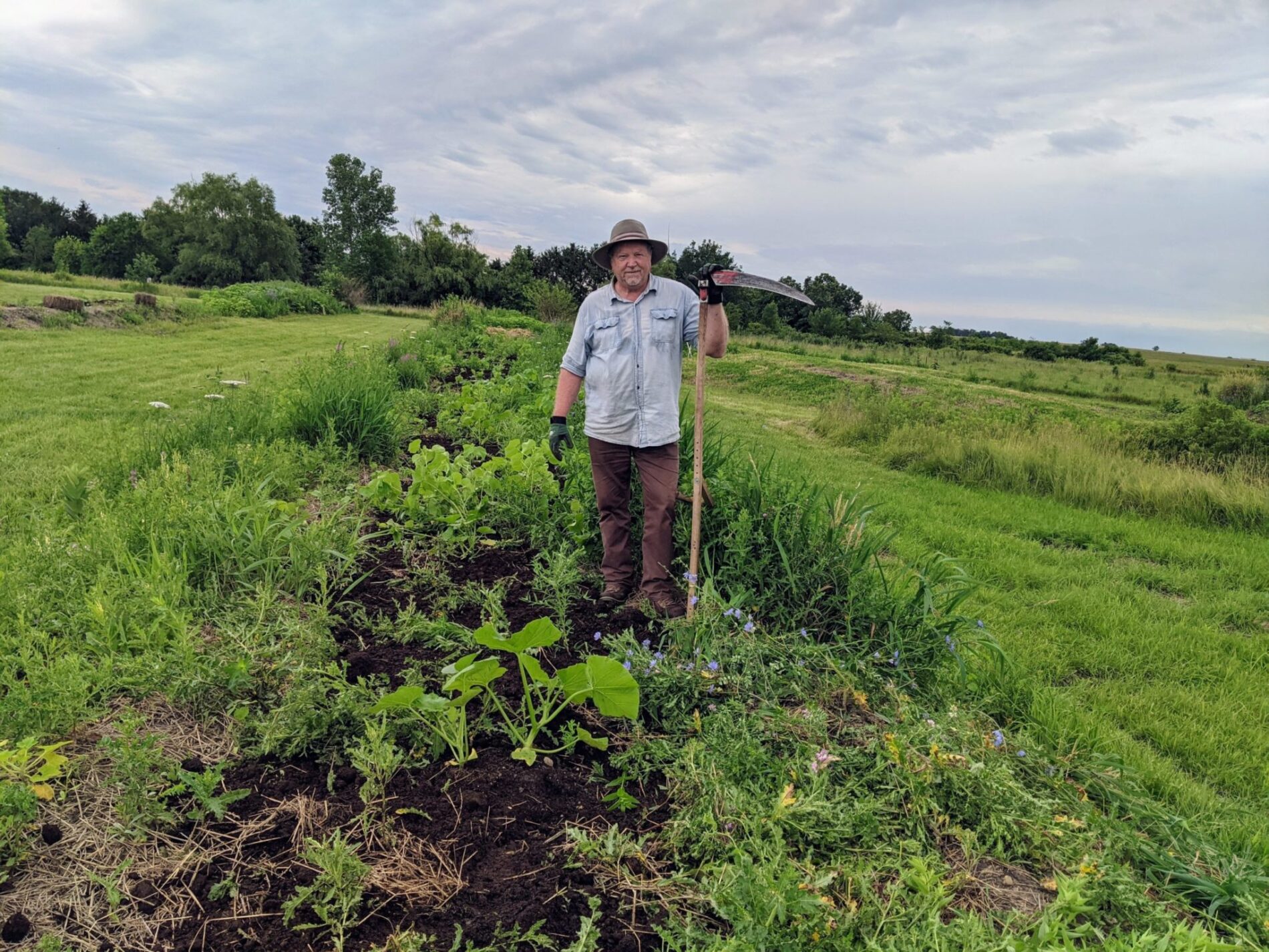 Bill Wilson with scythe cutting down weeds along a swale